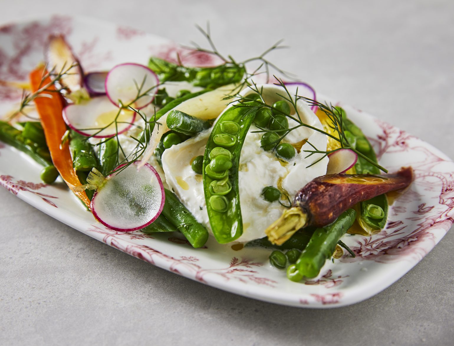 A spring salad of burrata, snap peas, peas, shaved radish and heirloom carrots with dill, on a pink toile platter